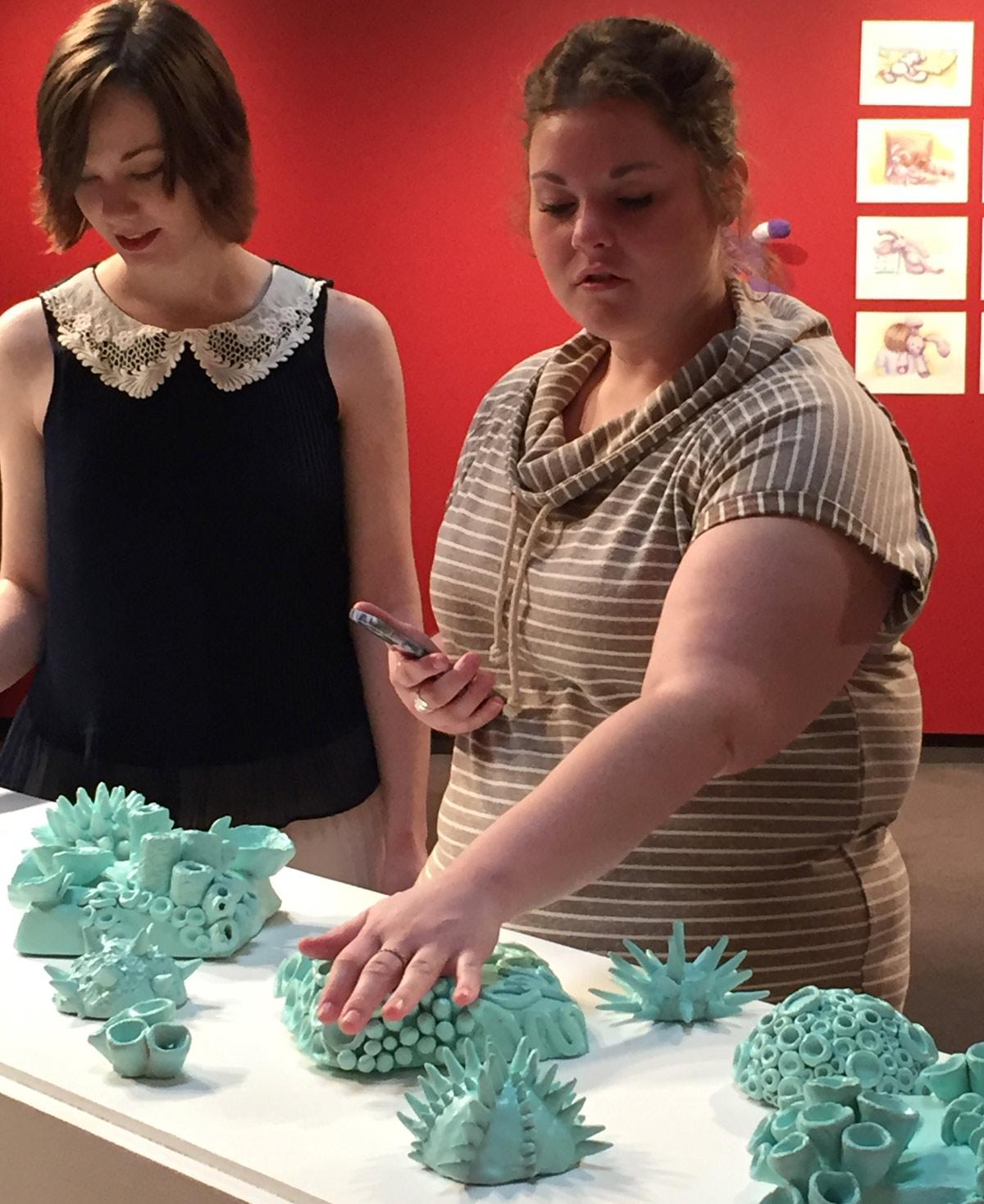 student touching a ceramics display at a gallery opening. 