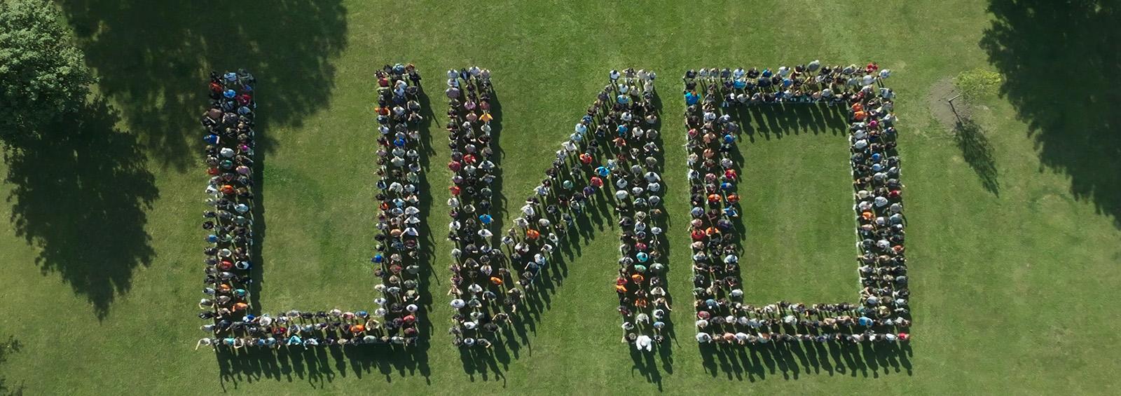 学生 & 工作人员站在草坪上拼写O un 